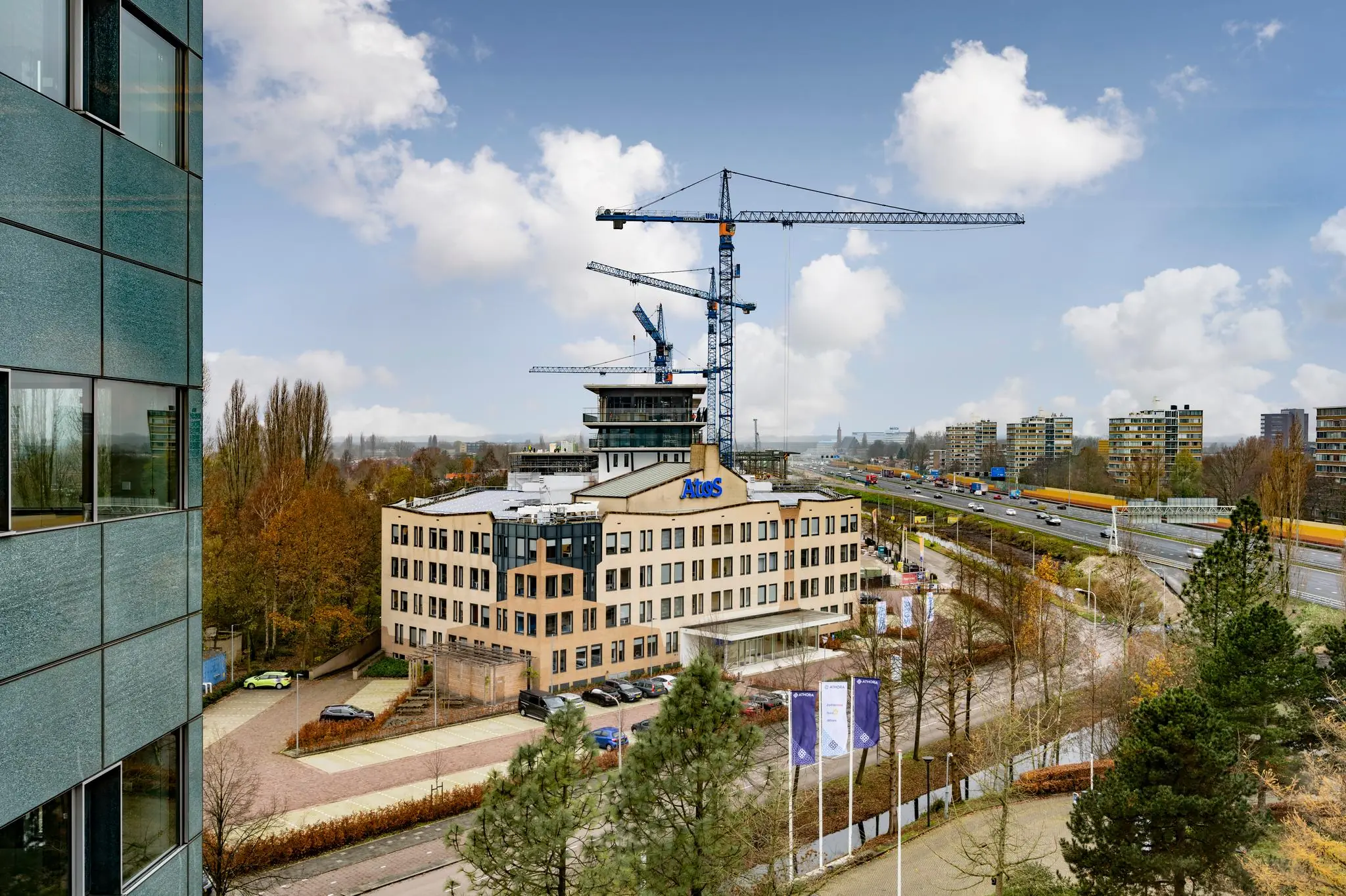 Kantoorgebouw van Atos aan de Burgemeester Rijnderslaan in Amstelveen met bouwkranen op het dak en zicht op de snelweg A9.